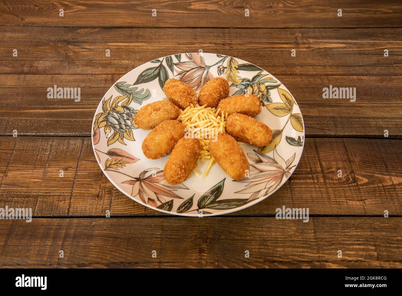 serving of Spanish croquettes filled with cream and Iberian ham accompanied by straw potatoes on a plate decorated with flowers on a beautiful wooden Stock Photo