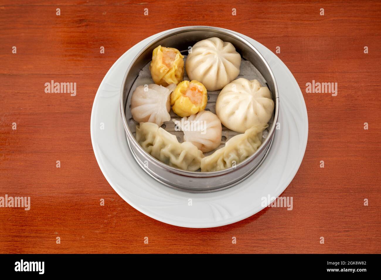Chinese dim sum and assorted Japanese gyozas steamed in characteristic metal container on white