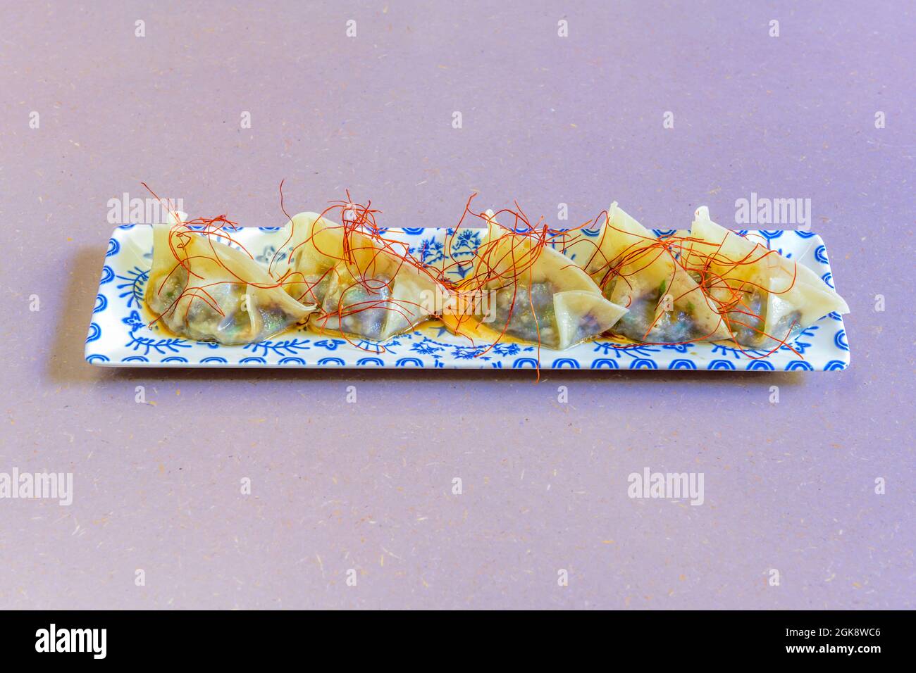 pretty long blue patterned tray with steamed stuffed dumplings with saffron strands on top Stock Photo