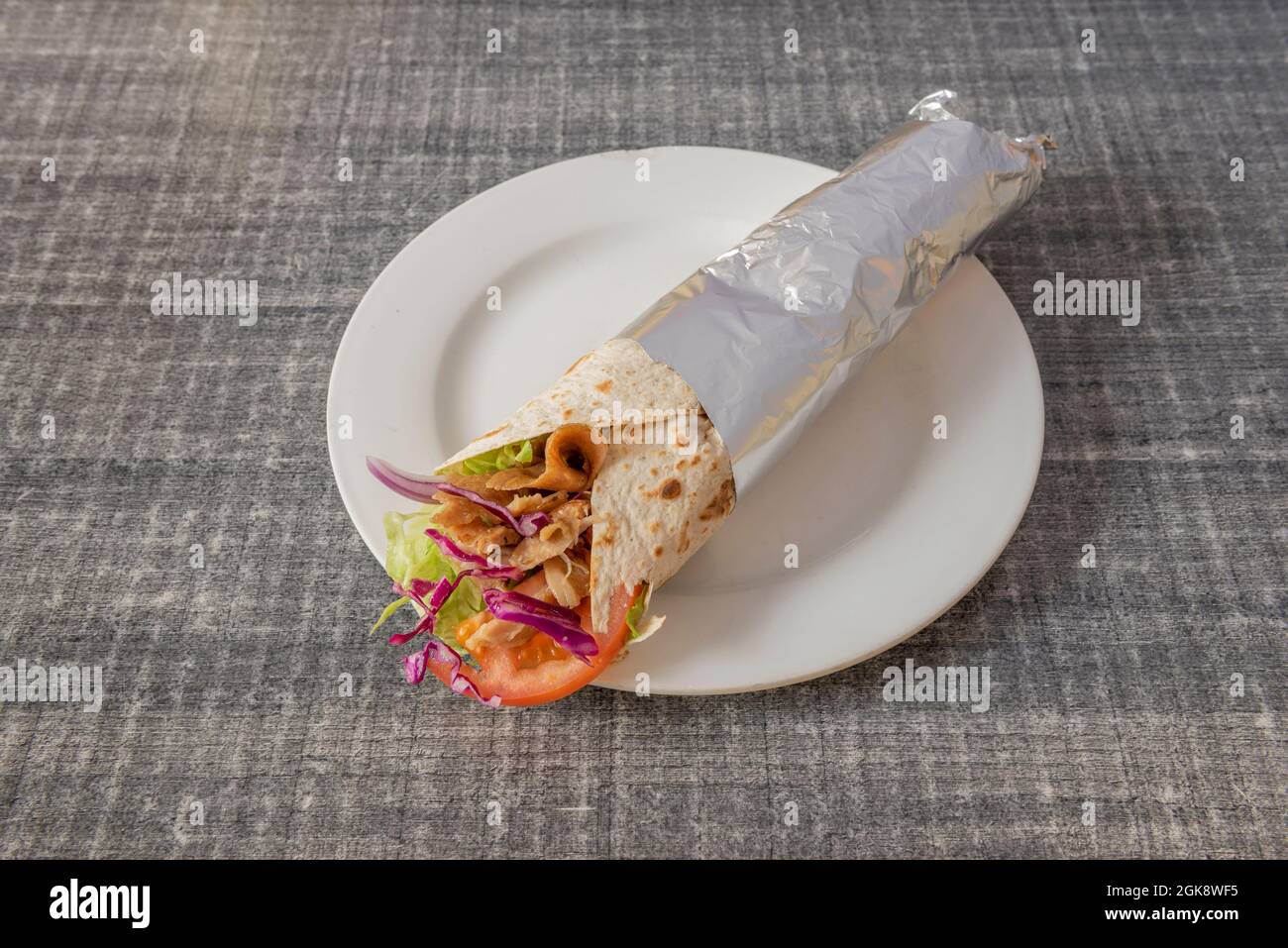 Durum typical of a popular kebab restaurant with lamb meat from the roll with red onion, kale, tomato and lettuce wrapped in aluminum foil Stock Photo