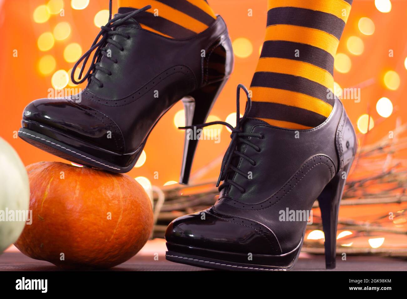 Witch legs in striped stockings and high heel shoes with Halloween pumpkins on an orange background with bokeh. Copy space. Stock Photo
