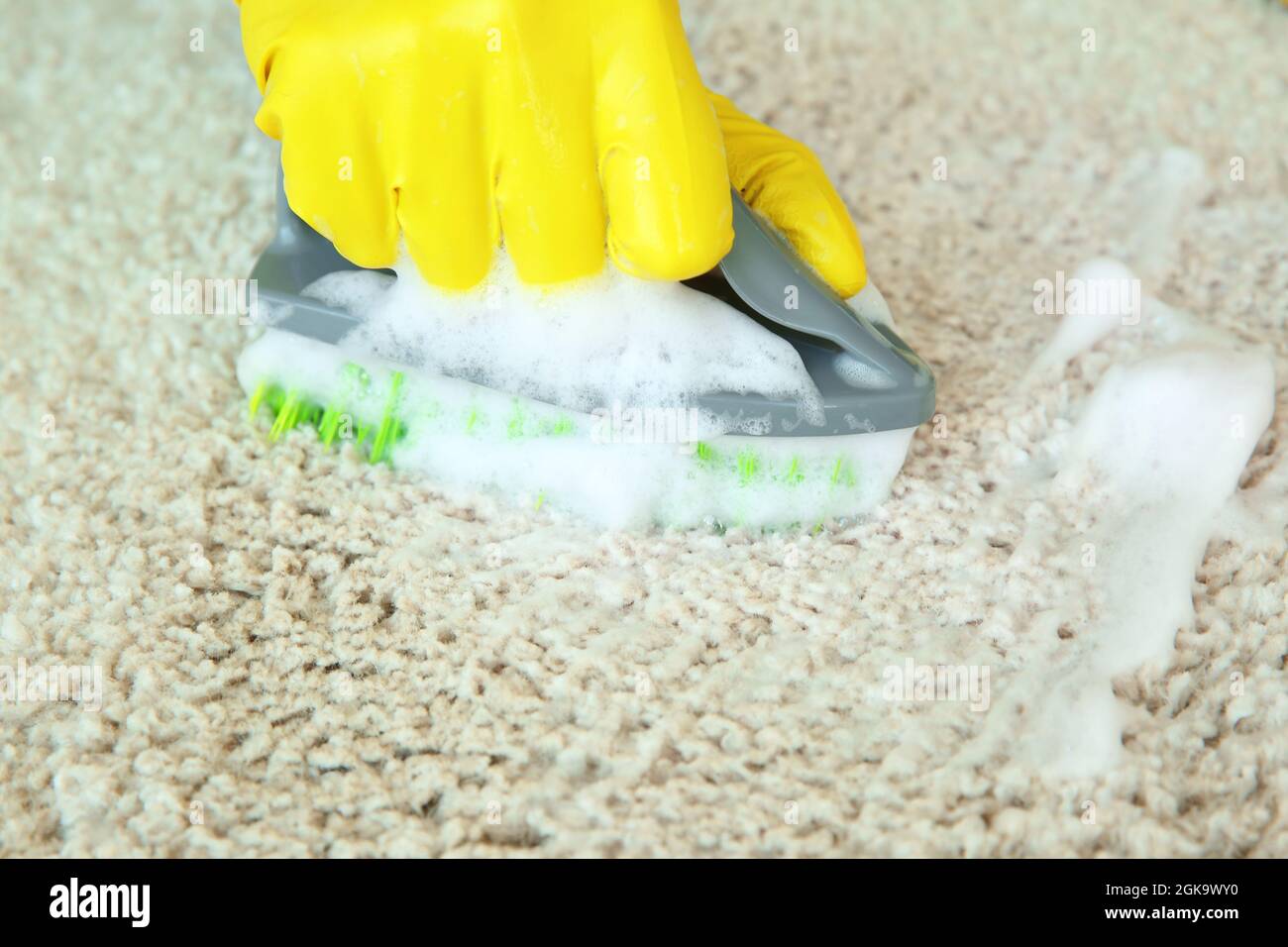 Hand in rubber glove cleaning carpet with brush and detergent