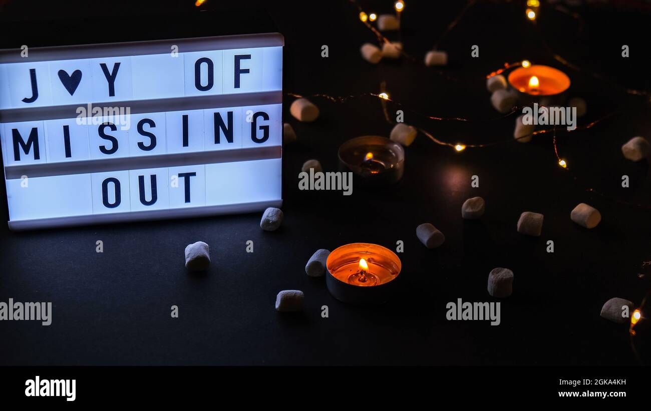 Lightbox with text JOMO Joy of Missing Out. The concept of relaxation from information and gadgets. Tea light candles. Digital detox Stock Photo