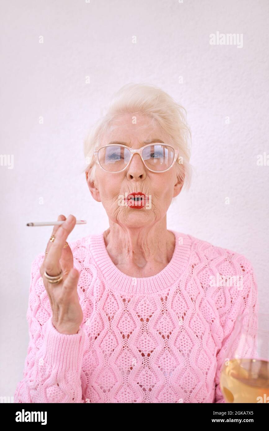 Old fashioned senior stylish woman smoking cigarette with glass of