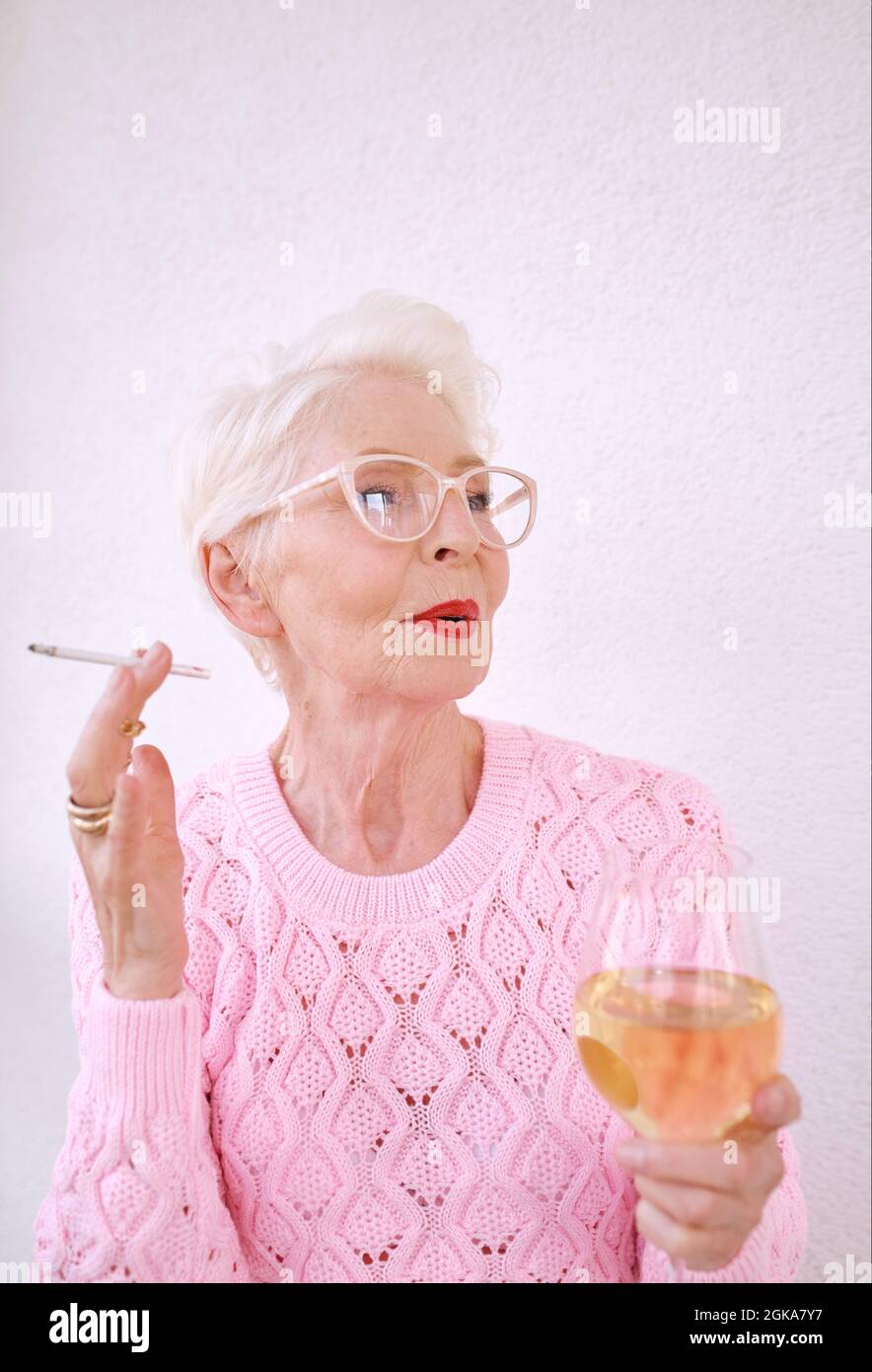 Old fashioned senior stylish woman smoking cigarette with glass of white wine. Bad habit, addiction concept Stock Photo
