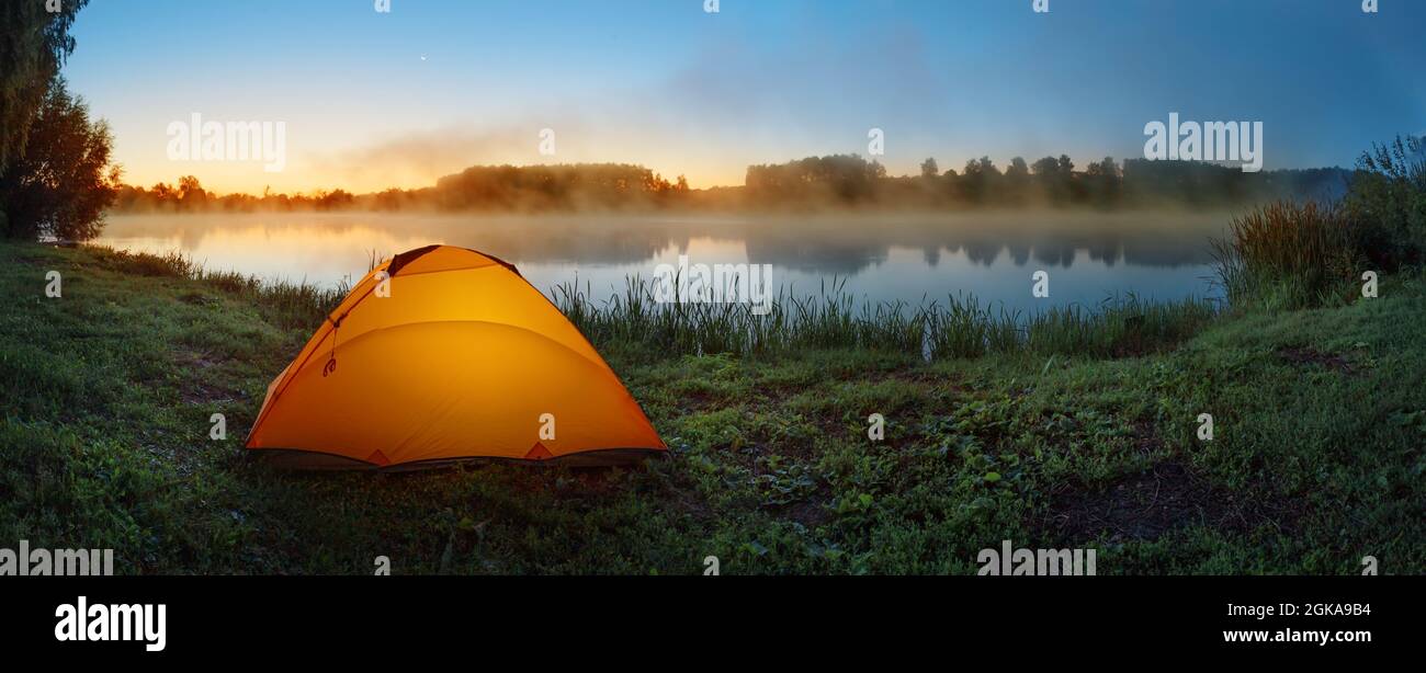 Orange tent on shore of misty lake at sunrise Stock Photo