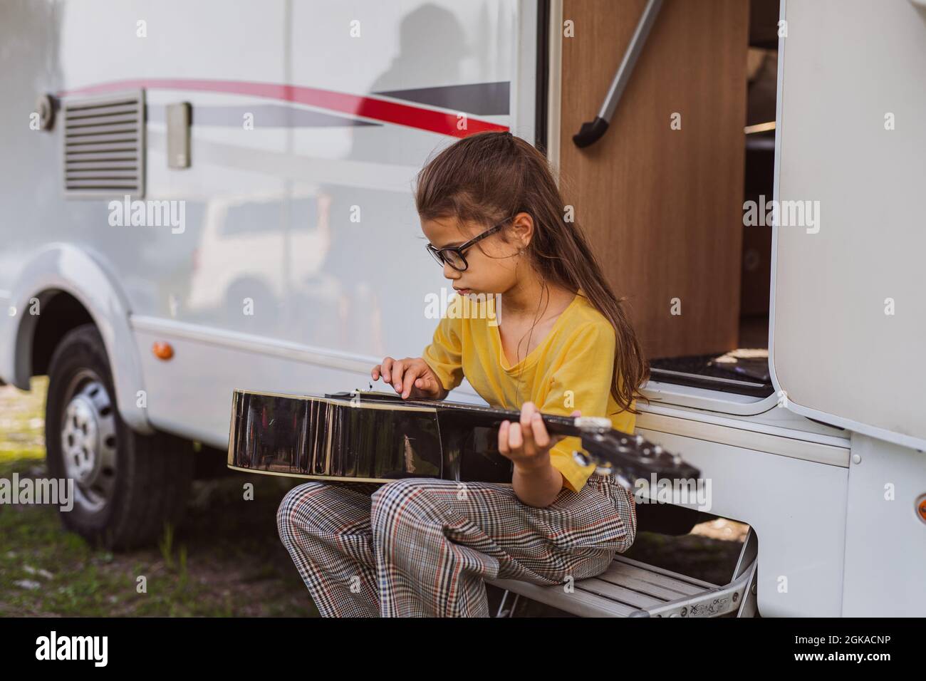 Small girl with guitar playing by caravan, family holiday trip. Stock Photo