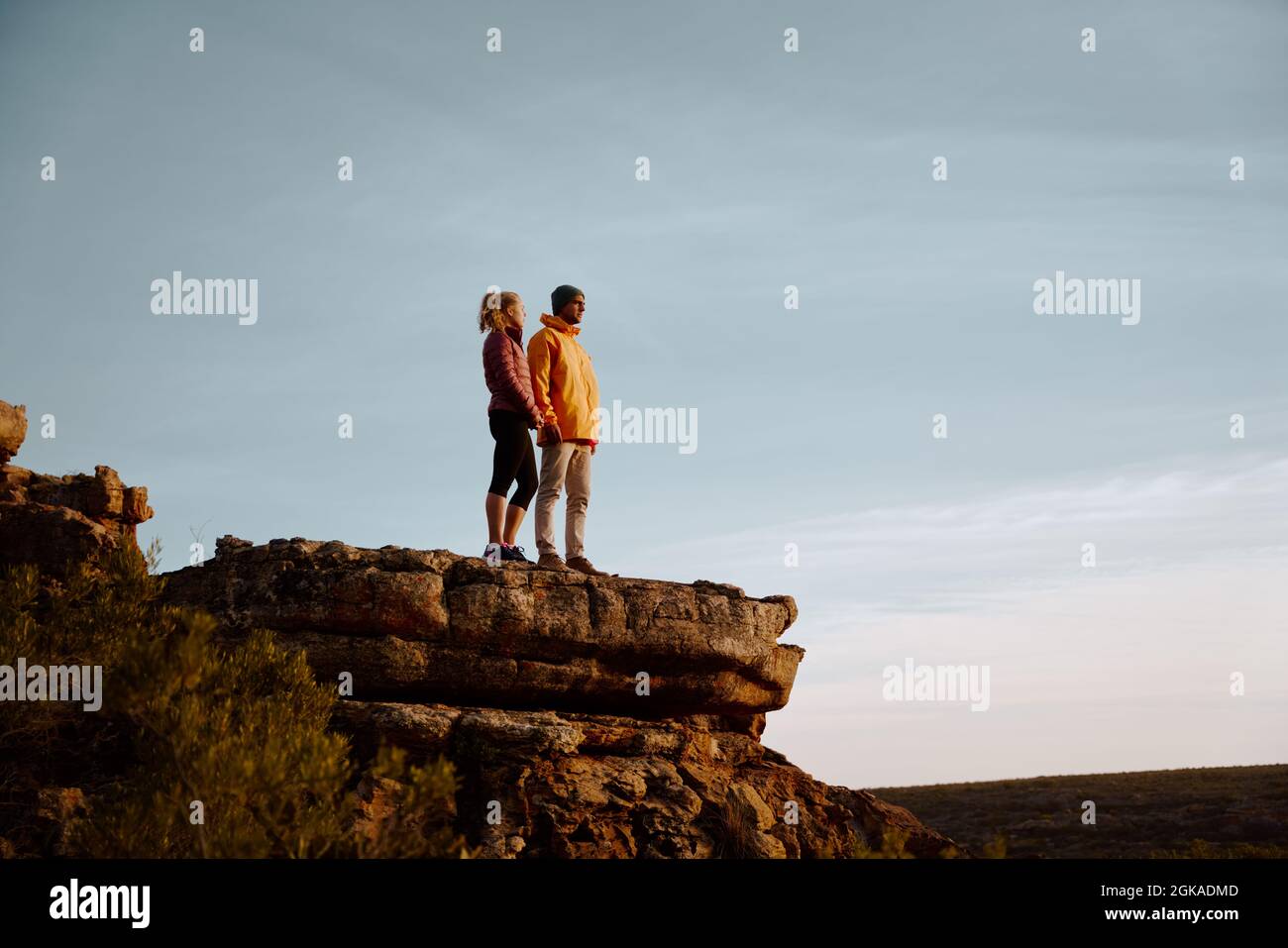 Young couple holding hands looking away standing at peak of cliff after ...