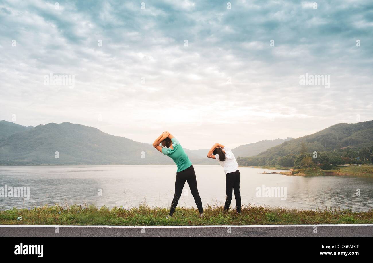 Mom and girl child doing stretching before workout outdoor at mountain lake in the morning to get a healthy lifestyle. Stock Photo