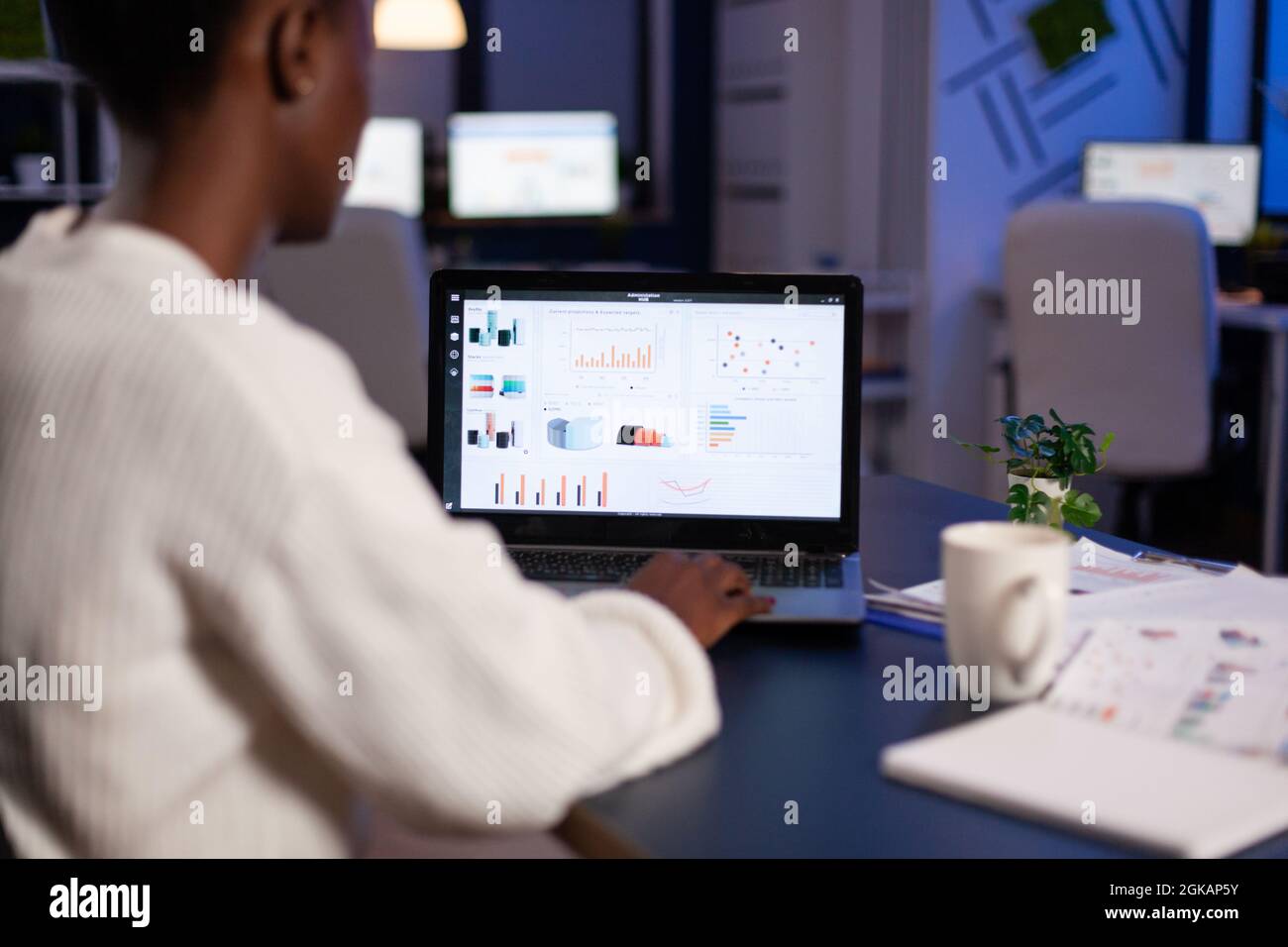 African american business entrepreneur analyzing financial company graphs on laptop computer overworking at annual reports late at night in startup office. Manager typing marketing statistics Stock Photo