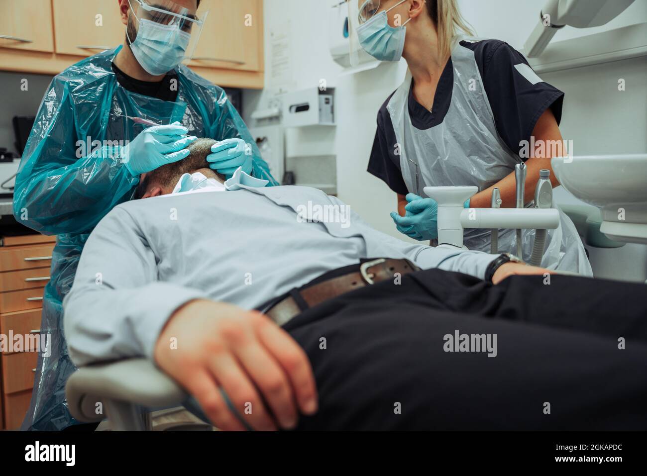 Caucasian male patient sitting on bed while male nurse examines inside of mouth using density tools Stock Photo