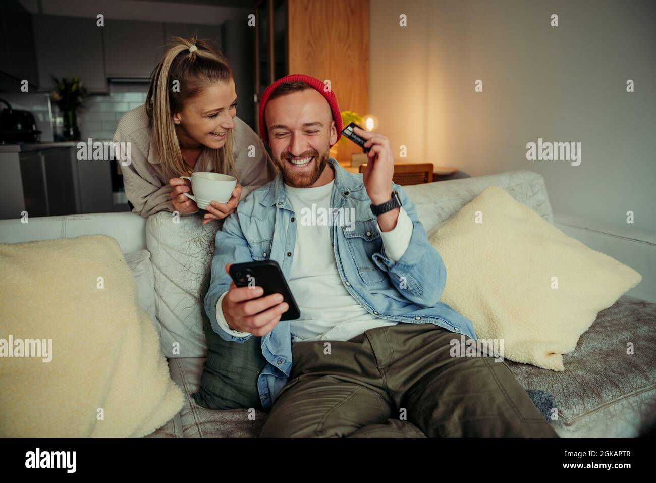Caucasian couple sitting on couch drinking coffee making online payment using cellular device Stock Photo