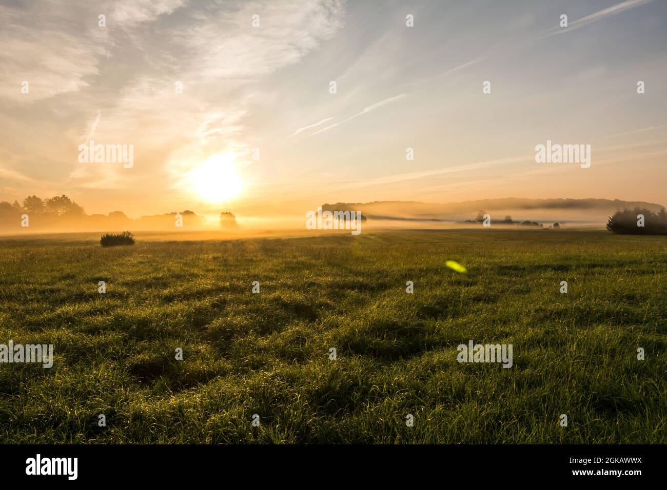 Beautiful sunset in rural landscape with sun rays shining through the morning fog Stock Photo