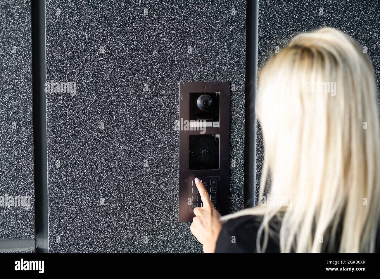 Happy woman ringing on doorbell at building entrance. Using intercom. Stock Photo