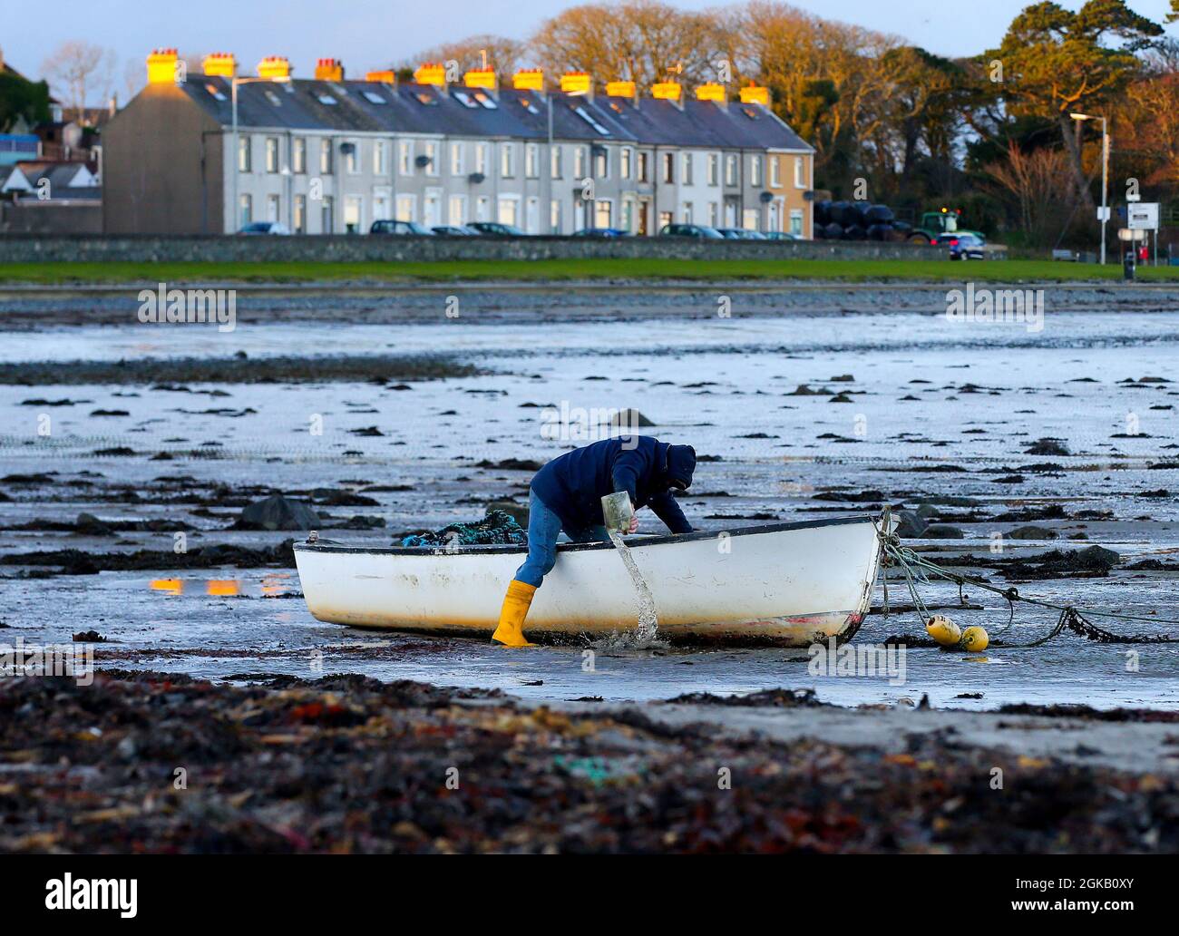 A fisherman bails out the excess water from his boat as the sun sets over the Irish Sea on Ballywalter Beach in Co. Down, Northern Ireland. Stock Photo