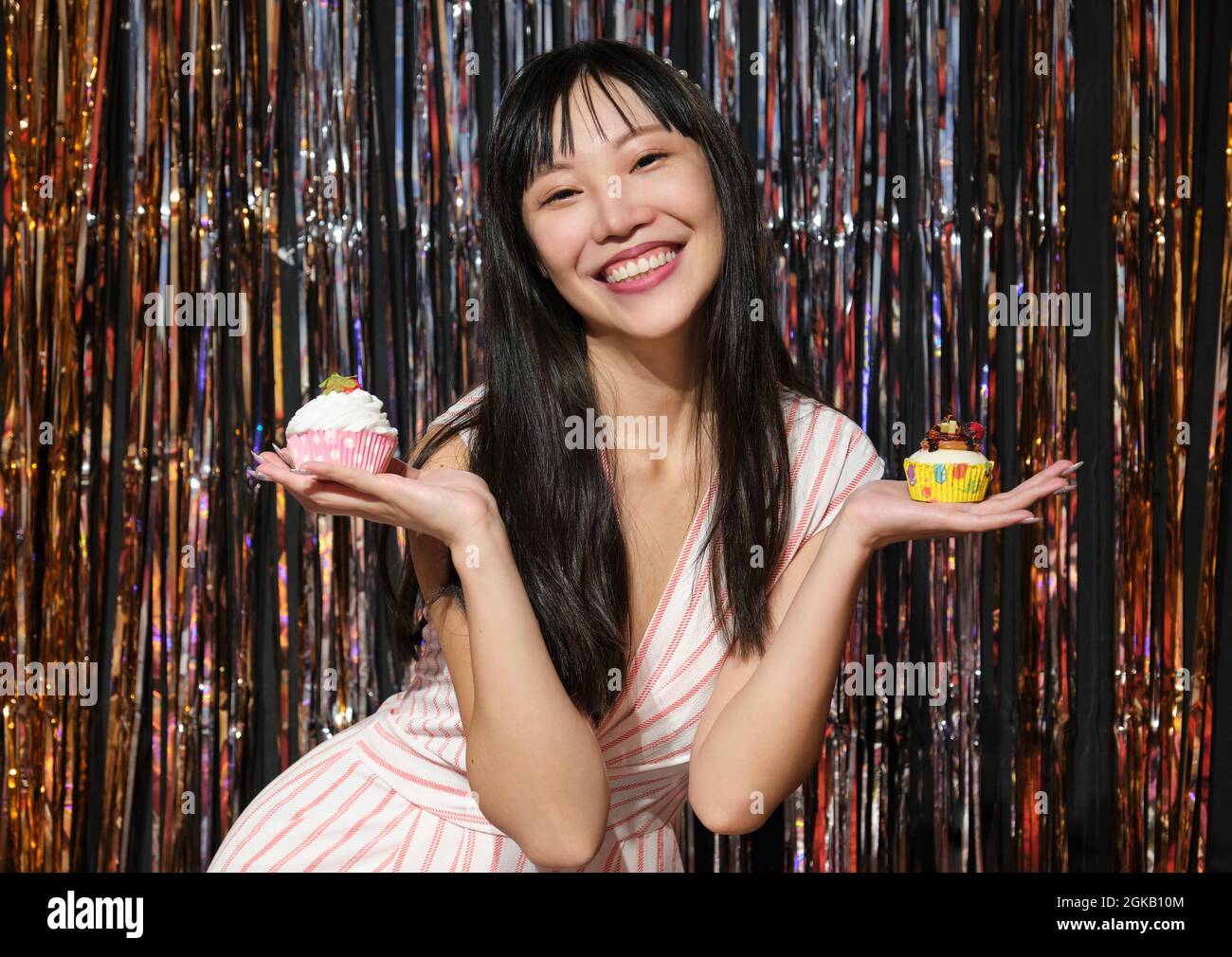 Young asian woman holds cupcakes in her hands over a party background. Stock Photo