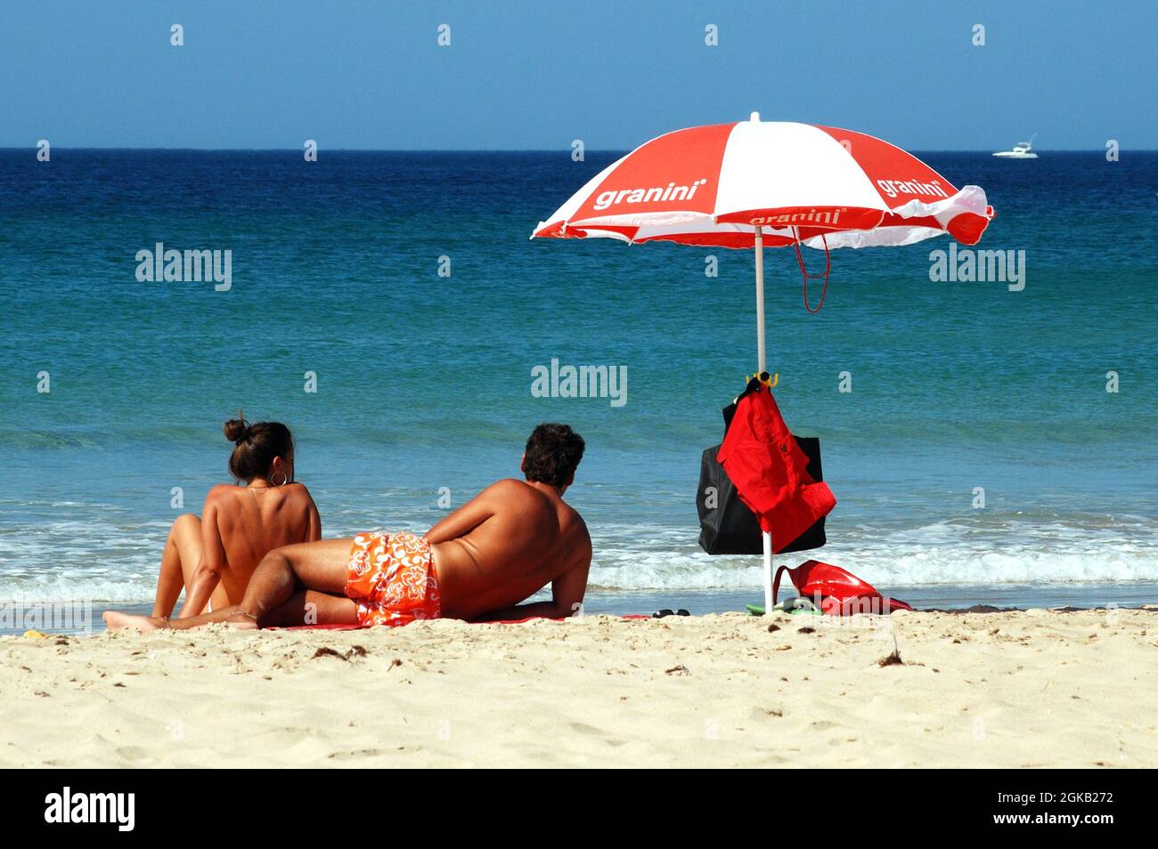 Young couple with a parasol sunbathing by the waters edge on the beach with views out to sea, Zahara de los Atunes, Spain. Stock Photo