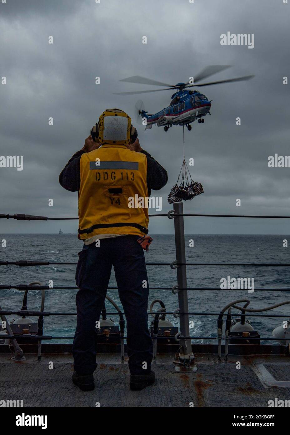 PACIFIC OCEAN (March 4, 2021) U.S. Navy Boatswain’s Mate Seaman Kyrese Robinson, from Sacramento, Calif., signals the pilot of an H225 Super Puma helicopter, assigned to the Military Sealift Command dry cargo and ammunition ship USNS Alan Shepard (T-AKE 3), from the aft missile deck of the Arleigh Burke-class guided-missile destroyer USS John Finn (DDG 113) during a vertical replenishment March 4, 2021. John Finn, part of the Theodore Roosevelt Carrier Strike Group, is on a scheduled deployment to the U.S. 7th Fleet area of operations. As the U.S. Navy’s largest forward-deployed fleet, 7th Fle Stock Photo