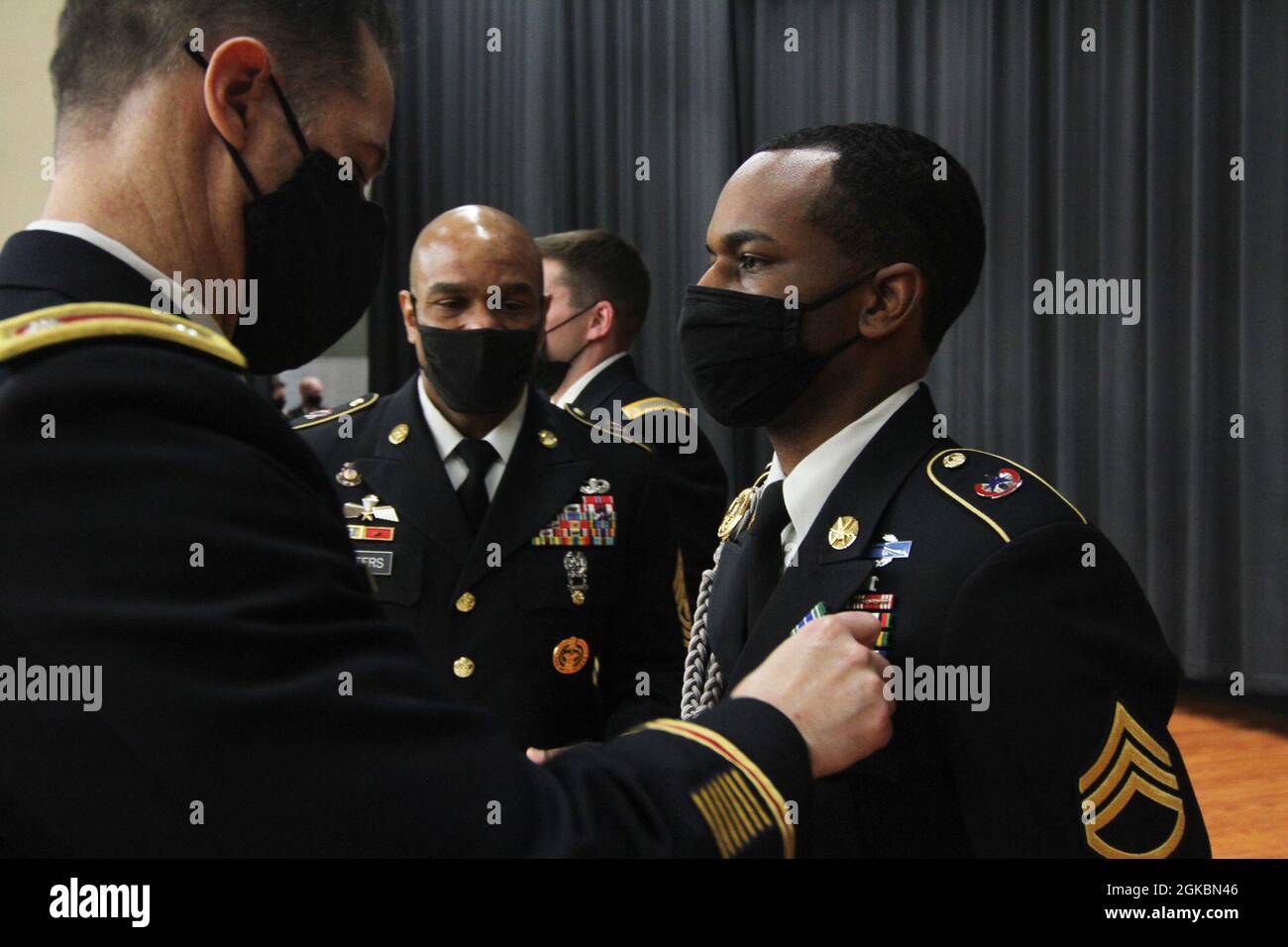 Lt. Col. Brian Kibitlewski, commander, Special Troops Battalion, 1st Theater Sustainment Command, and  Command Sgt. Major Sherman Waters Jr., senior enlisted advisor, STB, 1st TSC, pin the Army Achievement Medal to Staff Sgt. Nahjier Williams, public affairs noncommissioned officer, 1st TSC, at Fort Knox, Kentucky, March 5, 2021. Williams earned the award for designing the 1st TSC holiday card which won first place in the “People’s Choice” category during the Fort Knox holiday competition. Stock Photo