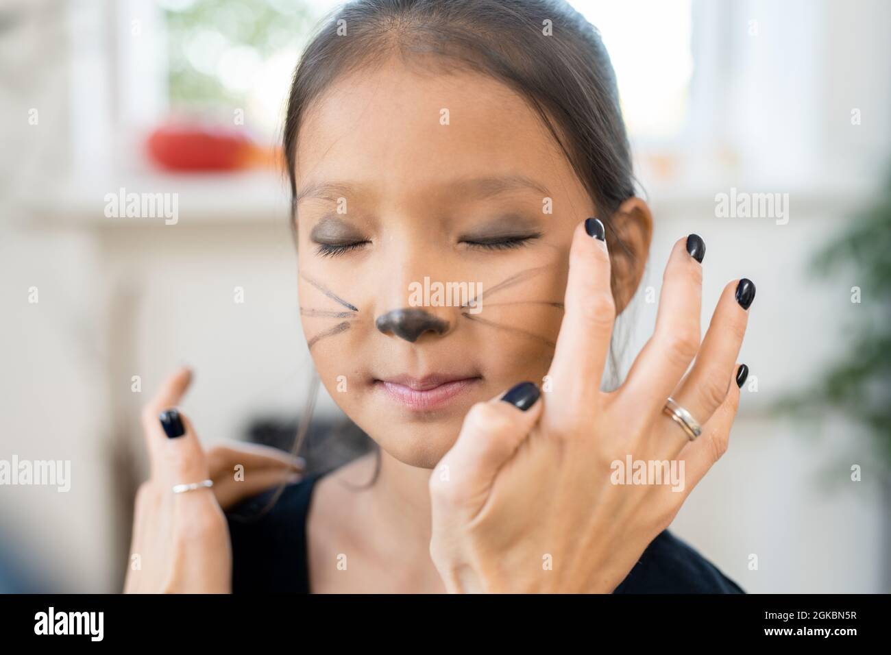 Little girl keeping eyes closed while woman applying dark grey eyeshadow on her eyelids for halloween Stock Photo