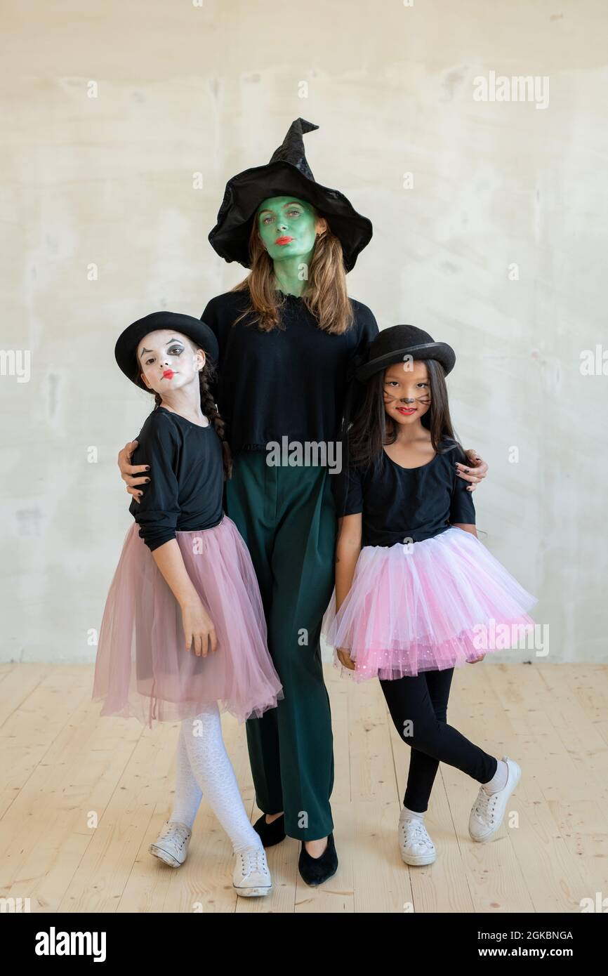 Young witch with her face painted green embracing two girls in pink skirts Stock Photo