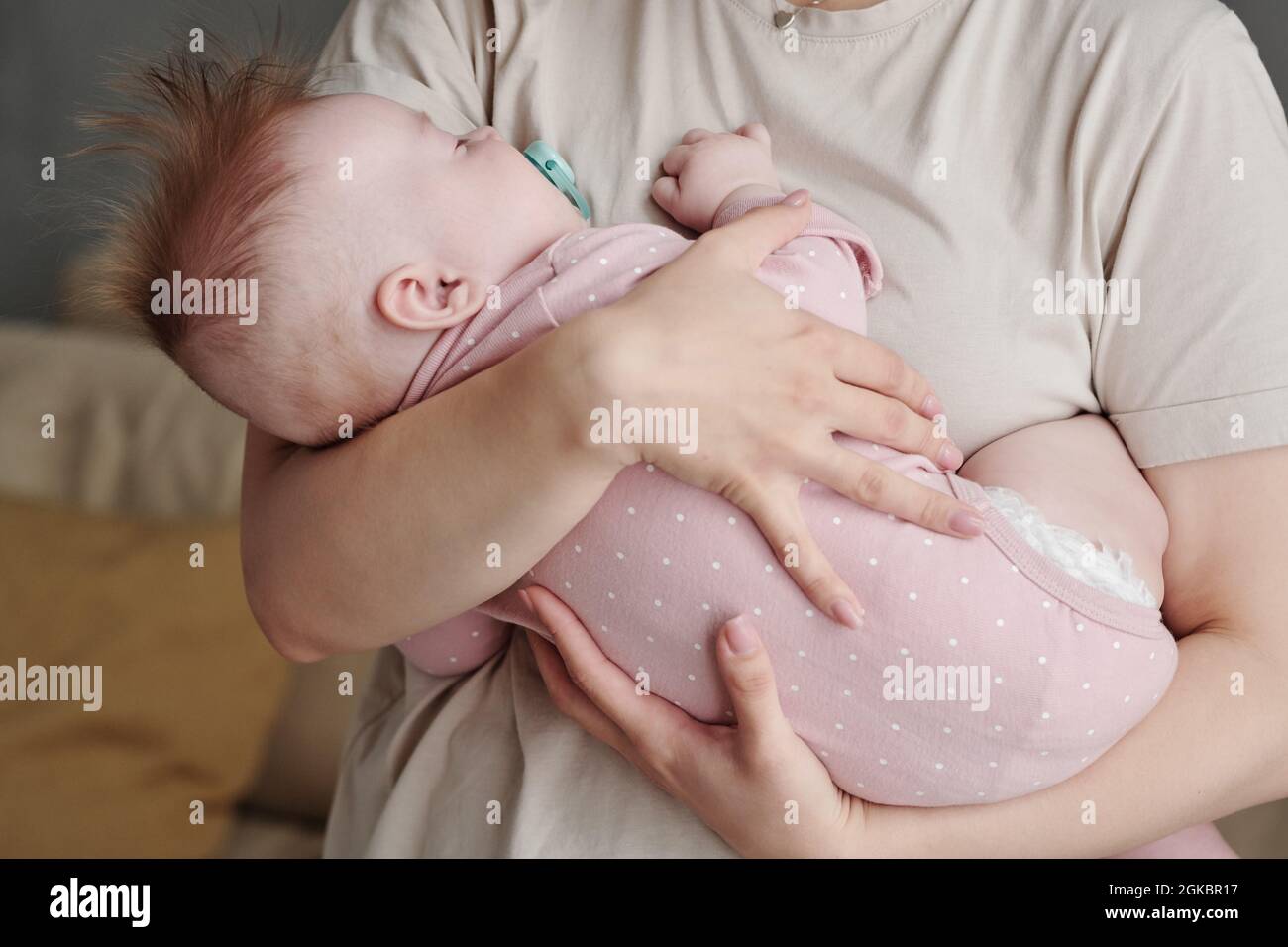 Adorable little baby with pacifier in mouth sleeping peacefully on hands of her mother Stock Photo