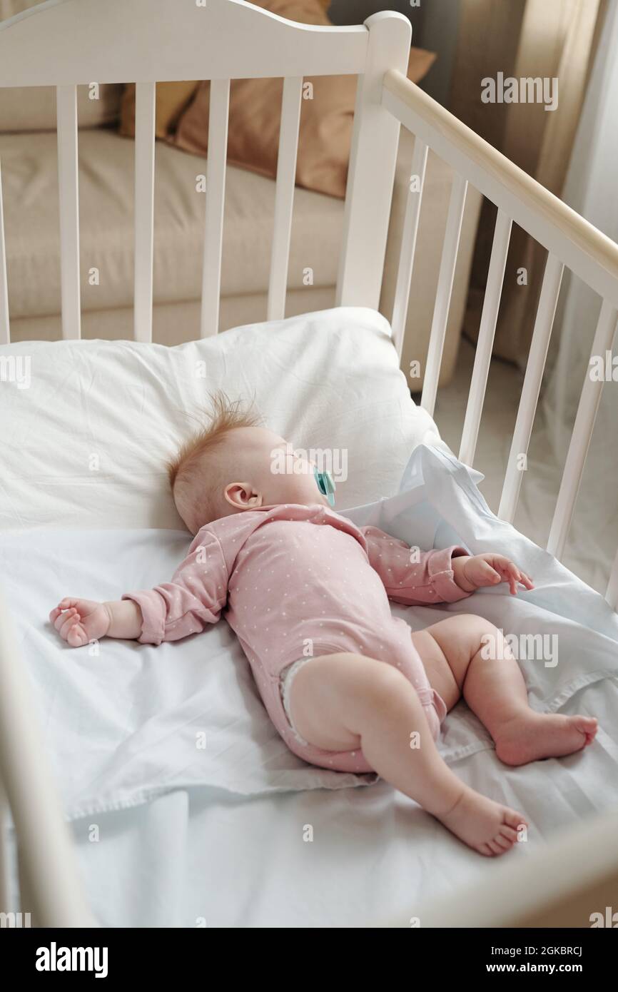 Adorable baby girl with pacifier in mouth sleeping peacefully in cradle Stock Photo