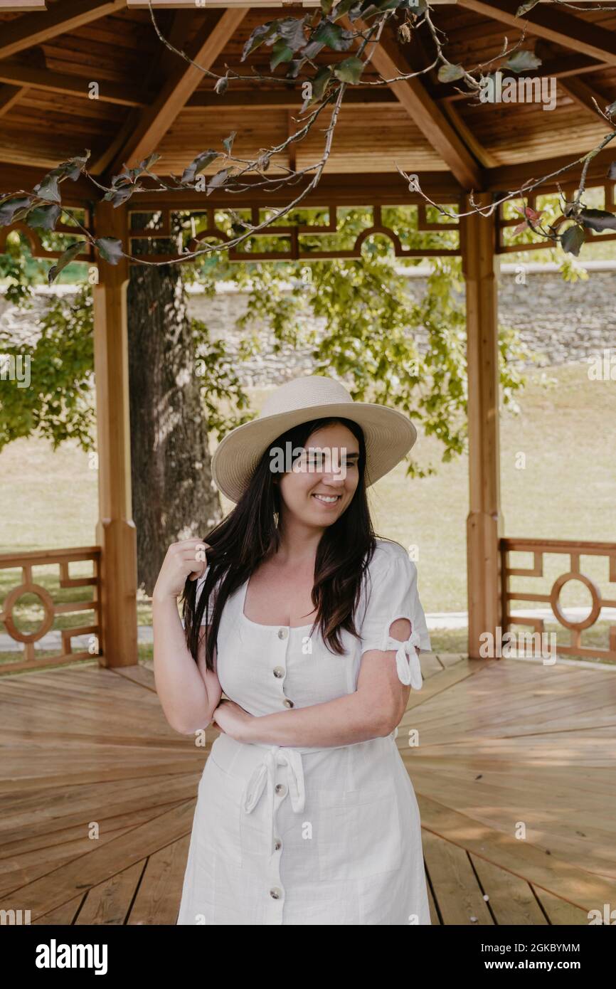 Happy young woman wearing white dress standing in front of pavilion in ...