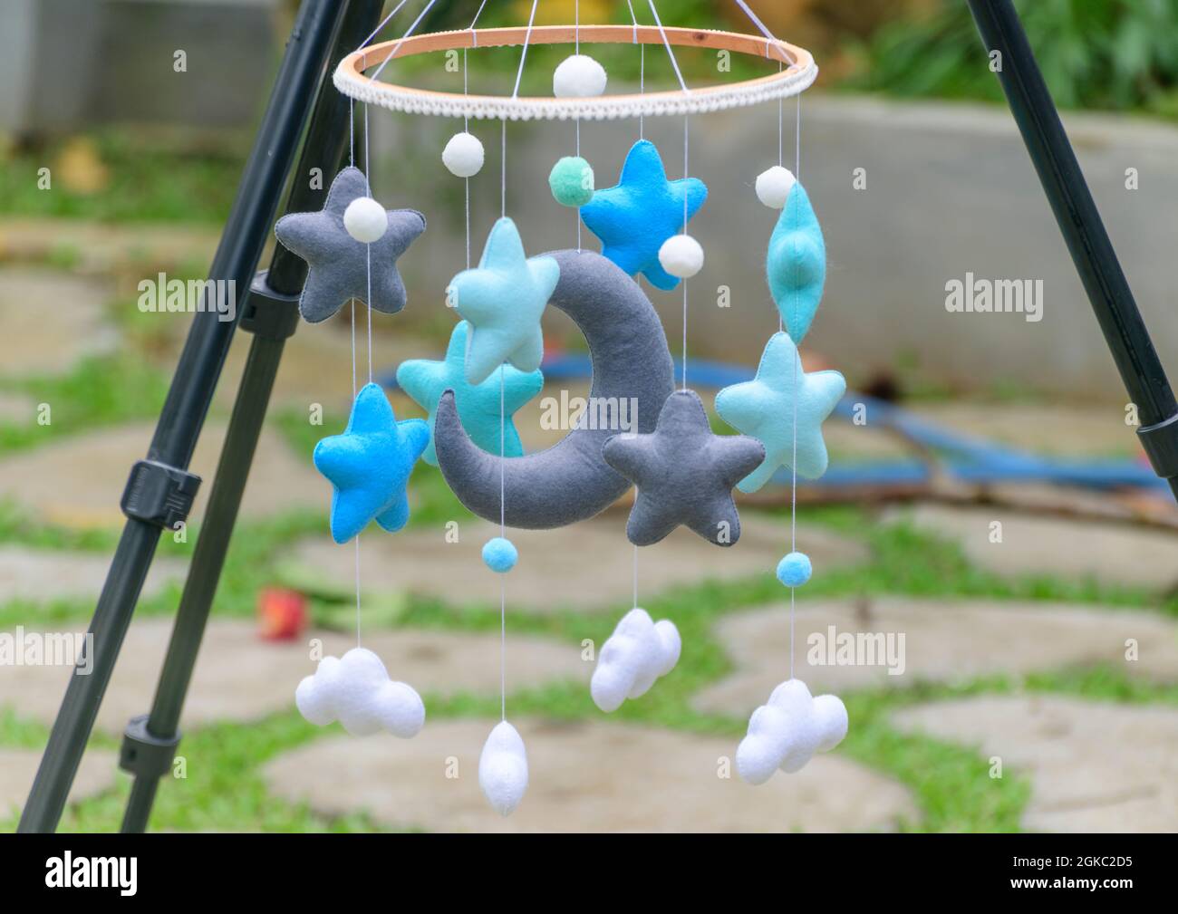 Baby cot mobile hangs from a camera tripod in the outdoor garden. Fluffy moon and star-shaped beautiful baby mobile. Stock Photo