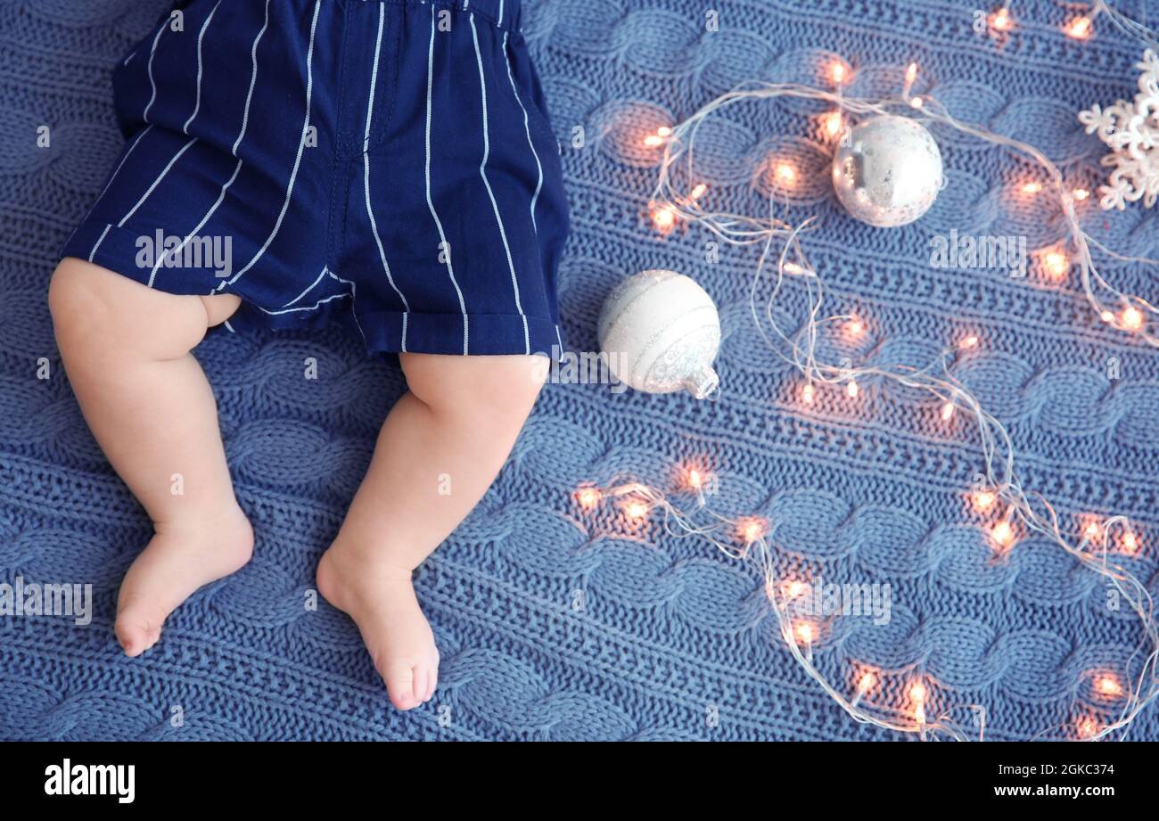 Cute little baby with Christmas lights and decorations on knitted
