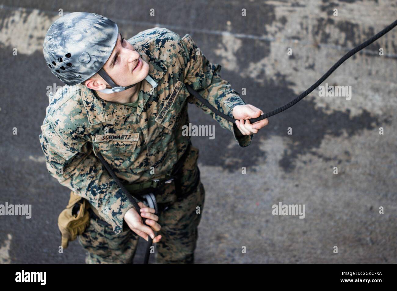U.S. Marine Lance Cpl. Carter Schwartz, an infantry rifleman with Kilo Company, Battalion Landing Team 3/4, 31st Marine Expeditionary Unit (MEU), stands as the belayer at the bottom of the rope during rappelling training aboard dock landing ship USS Ashland (LSD 48) on the shore of U.S. Naval Base Guam, March 10, 2021. The 31st MEU is operating aboard ships of Amphibious Squadron 11 in the 7th fleet area of operations to enhance interoperability with allies and partners and serve as a ready response force to defend peace and stability in the Indo-Pacific region. Stock Photo