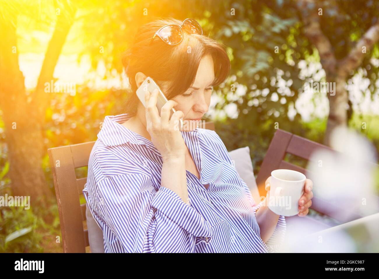Woman talking on the phone on smartphone in the garden hangs on hold while waiting Stock Photo