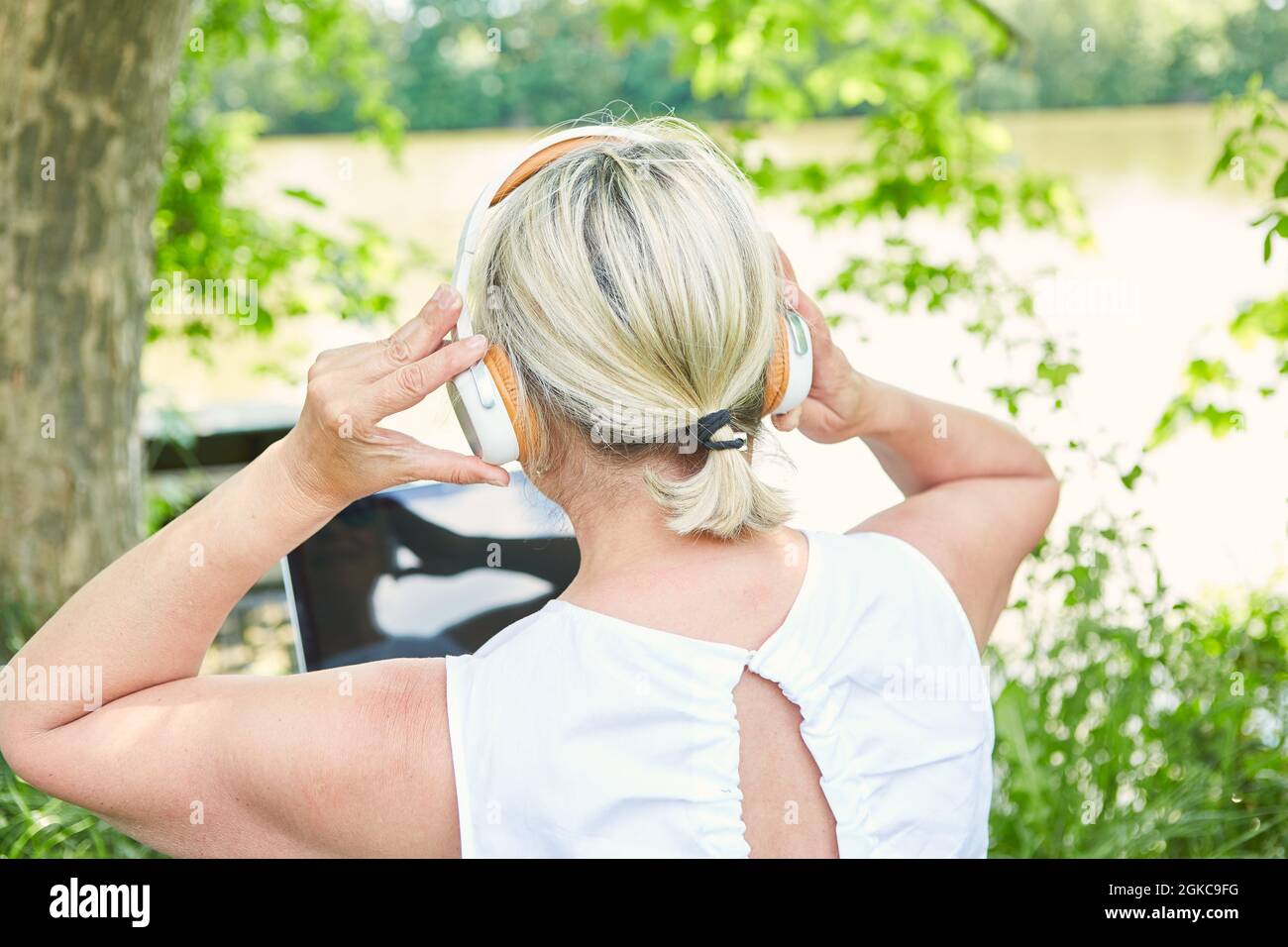 Business woman with headphones on laptop computer by the lake in nature as a freelancer Stock Photo