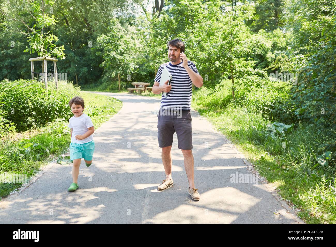 Single father talking on mobile phone with son in green park on vacation Stock Photo