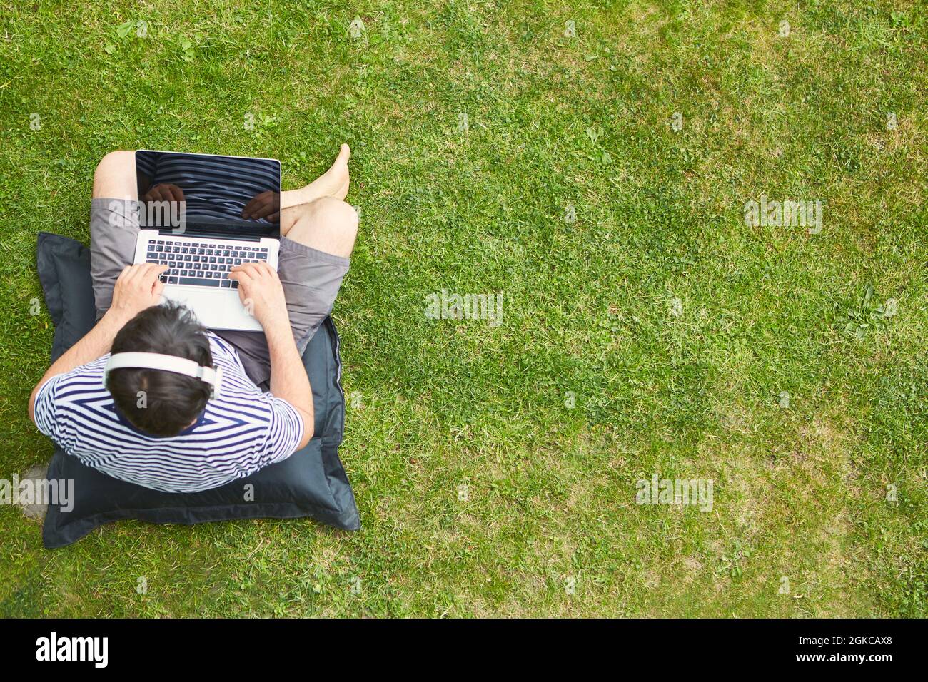 Man working as a freelancer on the lawn in the garden with laptop during a video conference Stock Photo