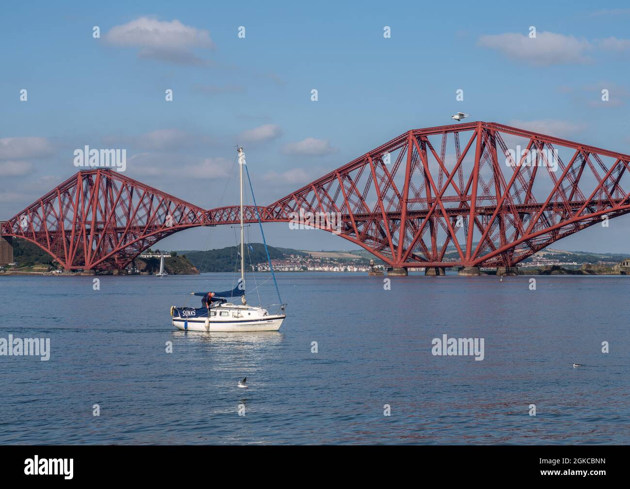 South Queensferry, Edinburgh, Scotland 7th September 2021 - A small sailing boat with the Forth Bridge in the background on a sunny day with clear sky Stock Photo
