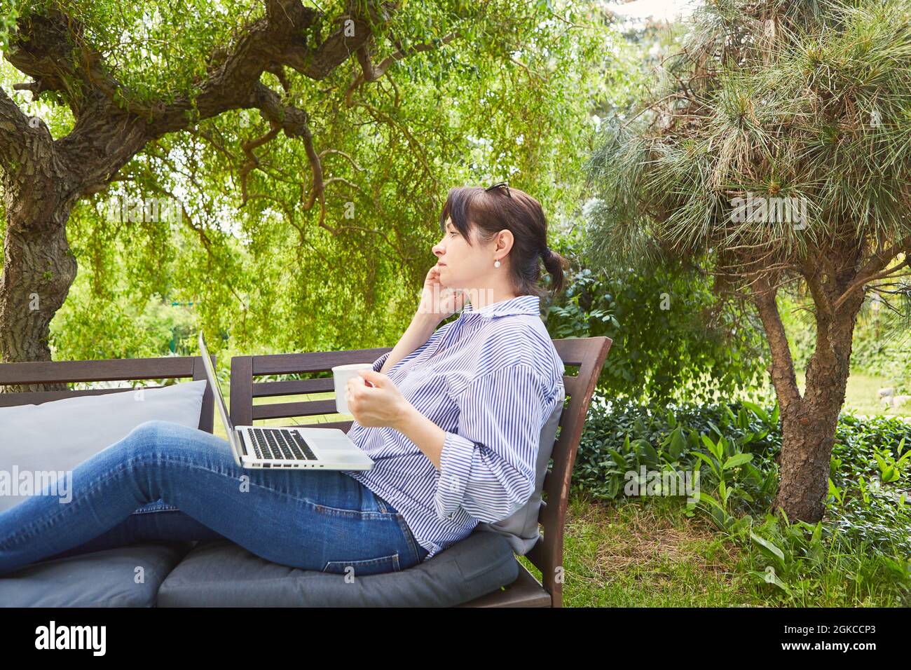 Business woman on vacation in the garden drinking a cup of coffee and talking on the mobile phone Stock Photo