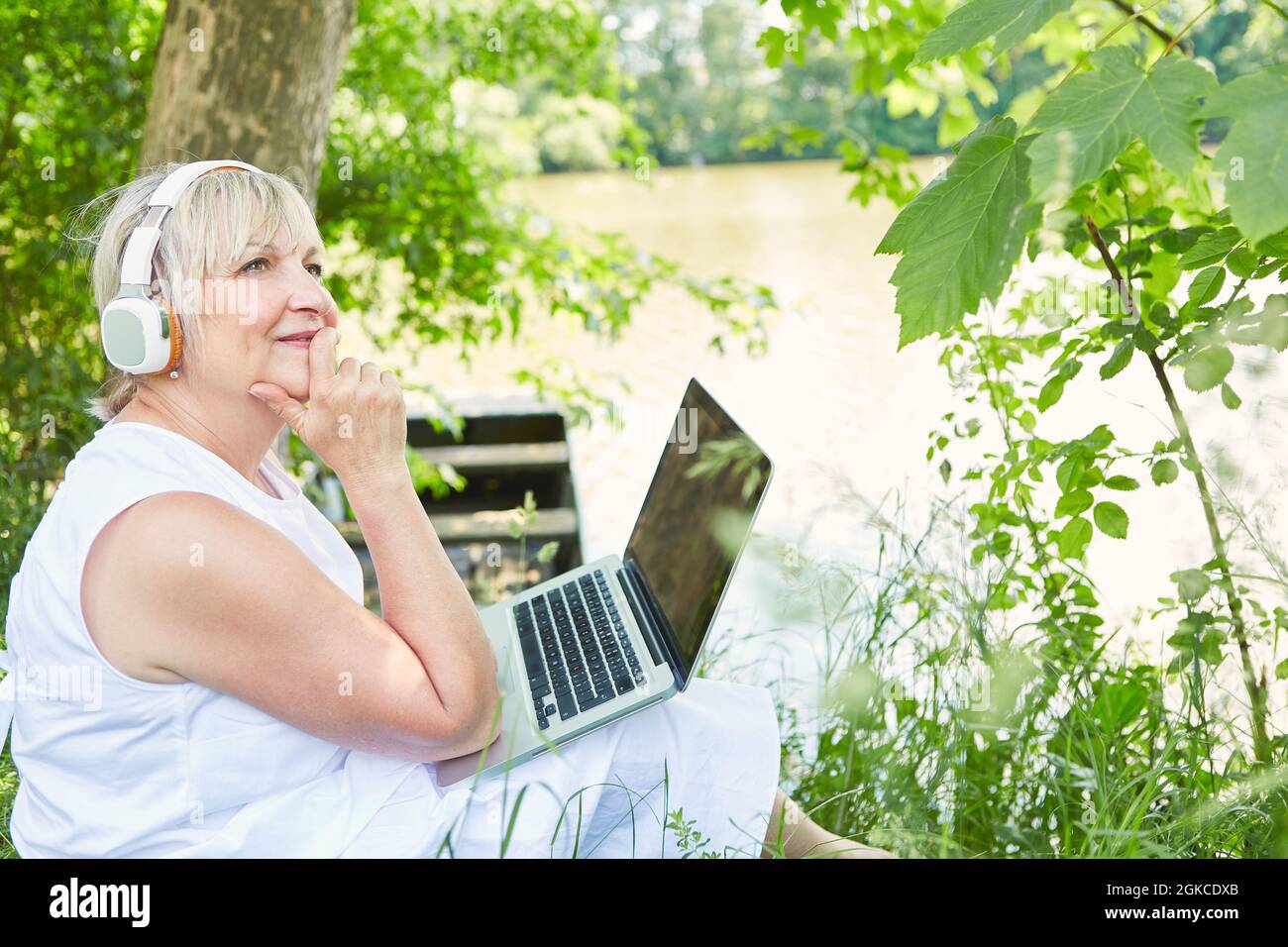 Business woman as a freelancer sits daydreaming at the laptop PC in the garden in nature Stock Photo