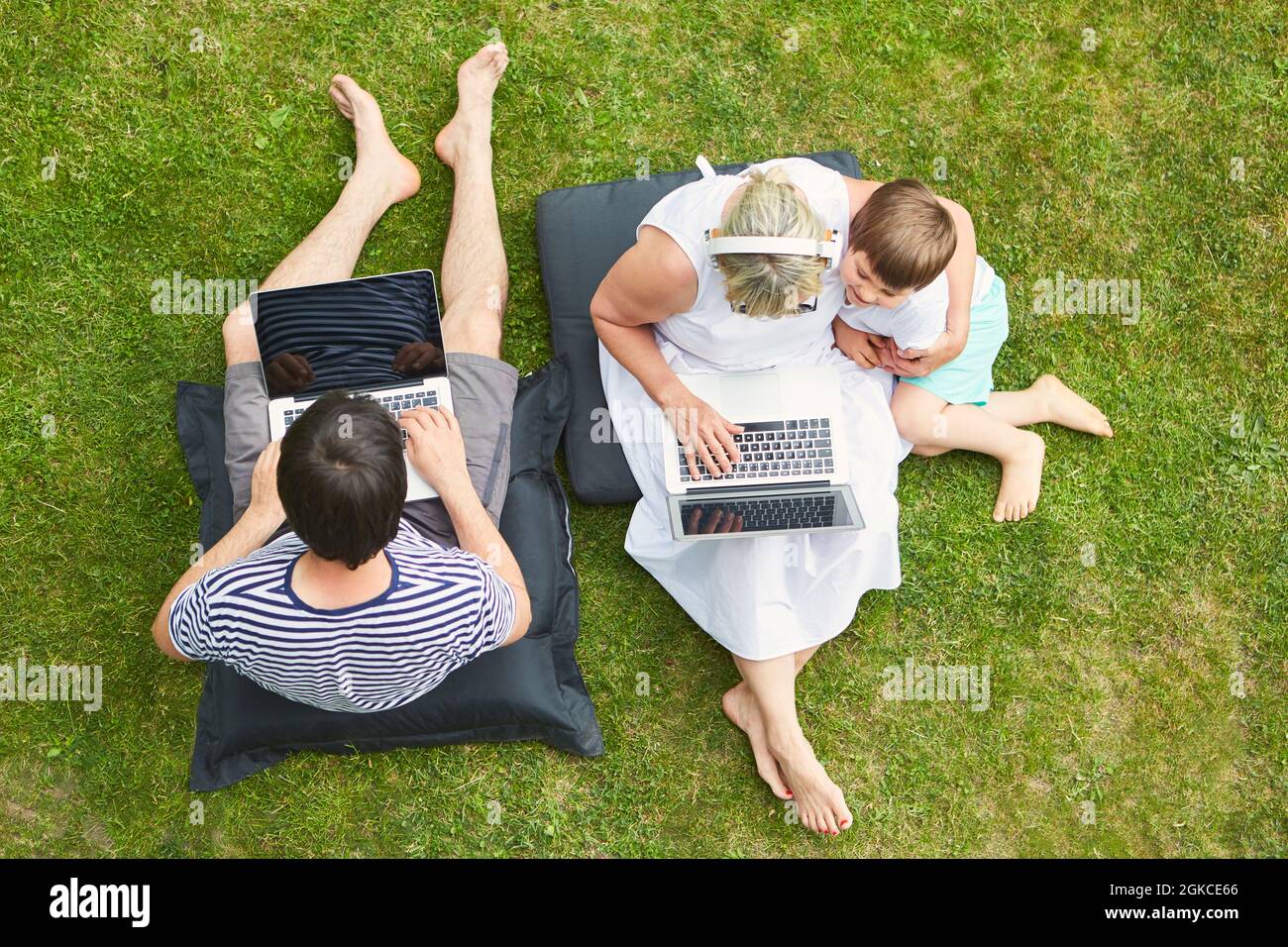 Curious child and parents at the laptop computer on the lawn in the garden on vacation Stock Photo