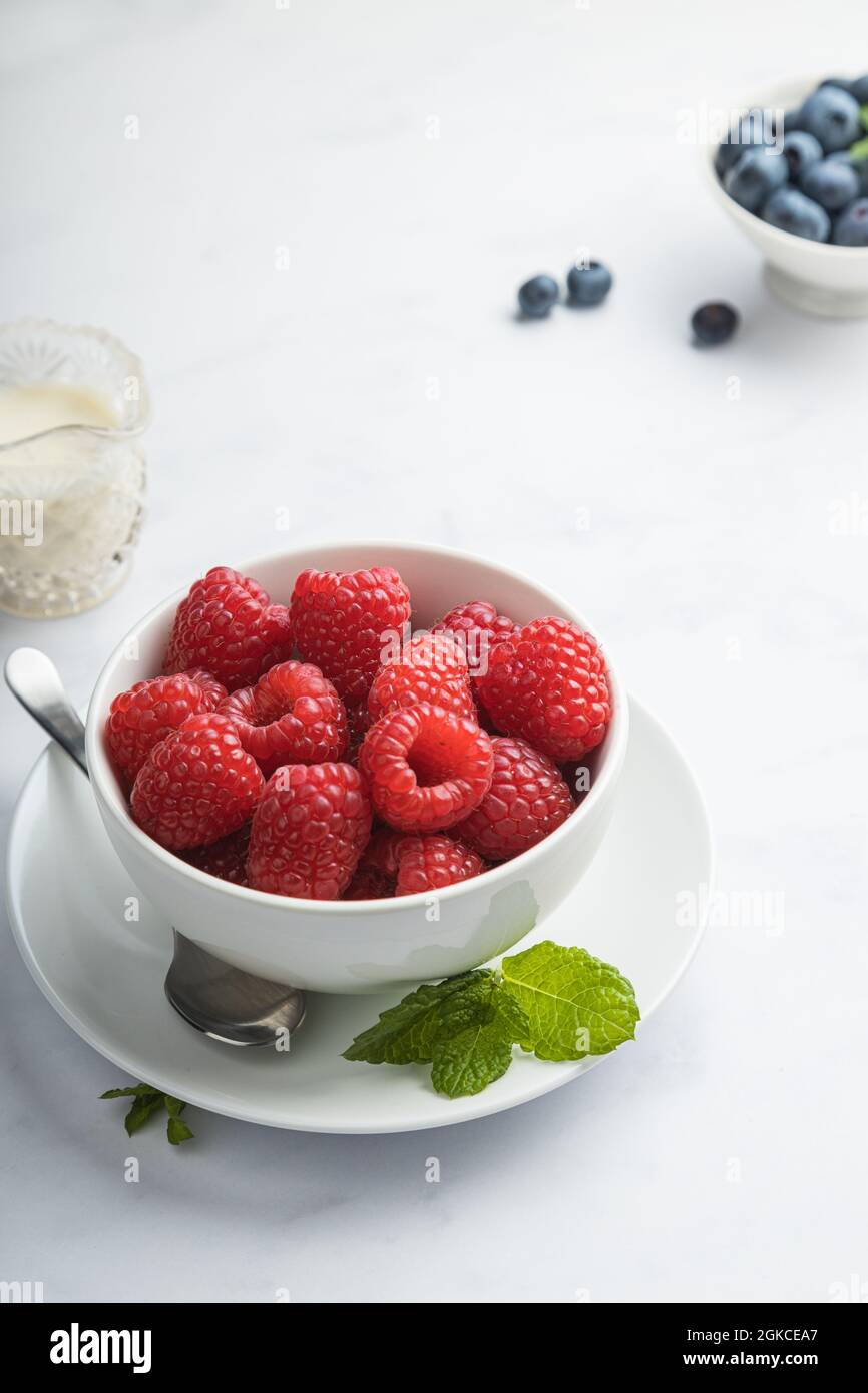 Bowl of fresh raspberries with blueberries, mint, and cream. Stock Photo