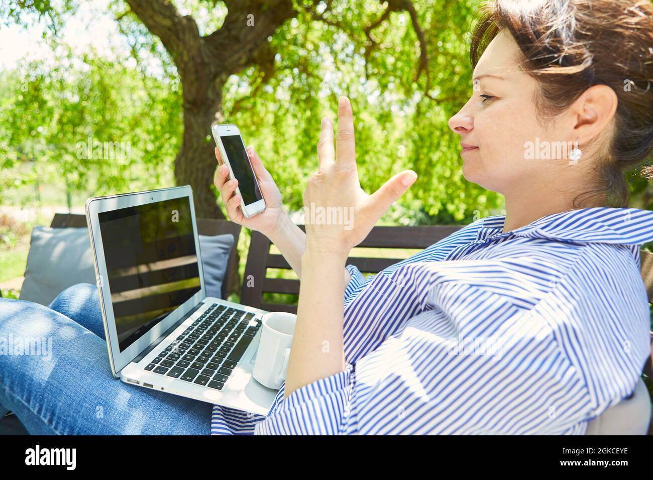 Freelancer woman using smartphone and laptop computer while watching video Stock Photo