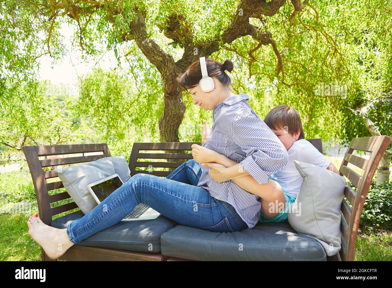 Mother at video conference on laptop PC in the garden is disturbed by child at work Stock Photo