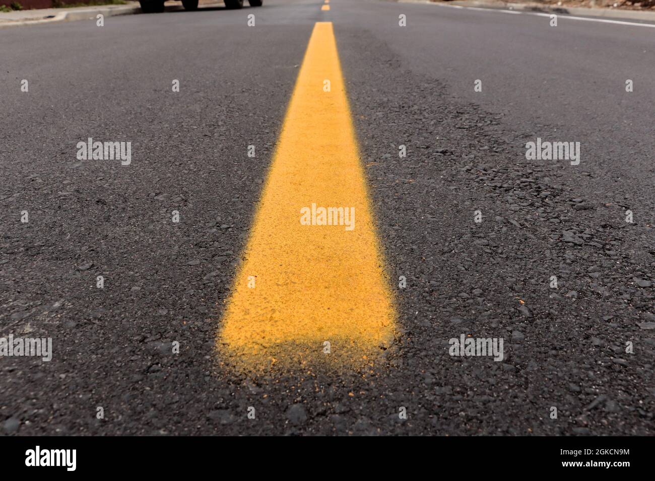 Asphalt track freshly made with some dirt and its texture, with a yellow strip painted in the center of the image and above the street horizon Stock Photo