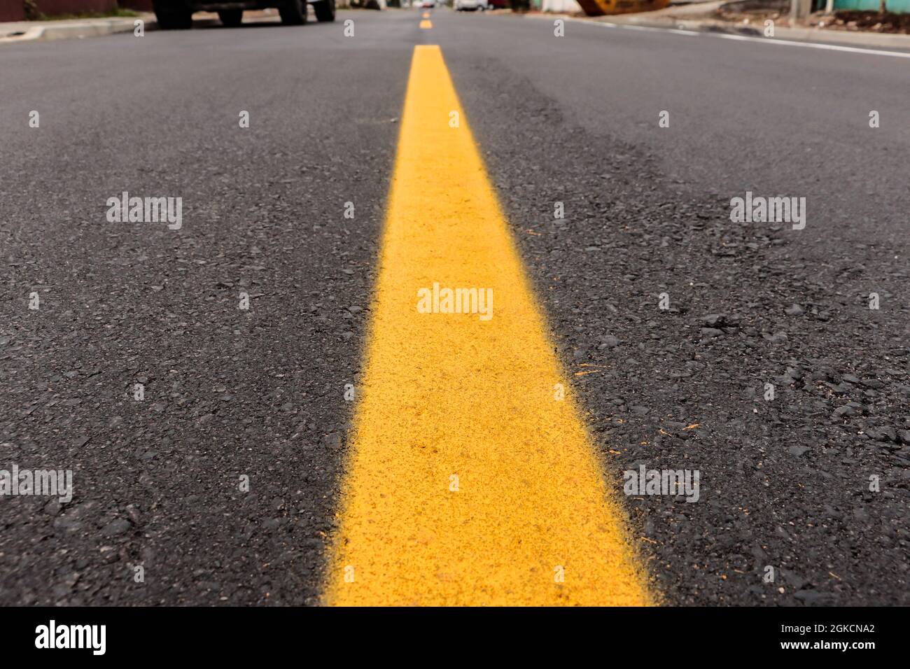Asphalt track freshly made with some dirt and its texture, with a yellow strip painted in the center of the image and above the street horizon Stock Photo