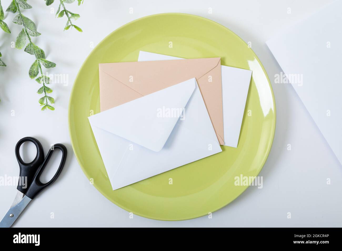 Composition of envelopes on green plate, scissors and branches on white background Stock Photo