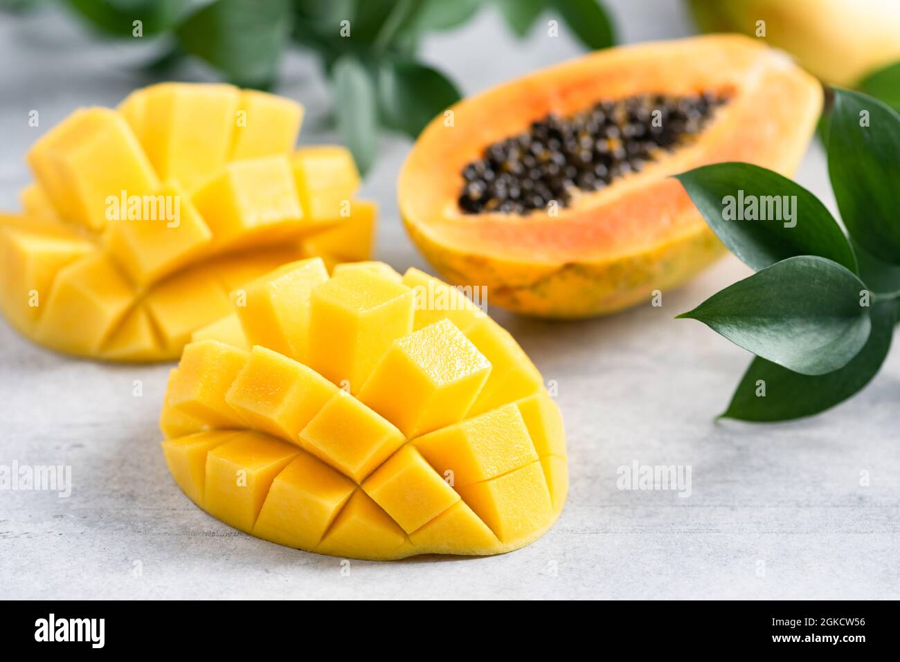Sweet ripe mango and papaya tropical fruit cut in half on grey concrete background closeup view Stock Photo