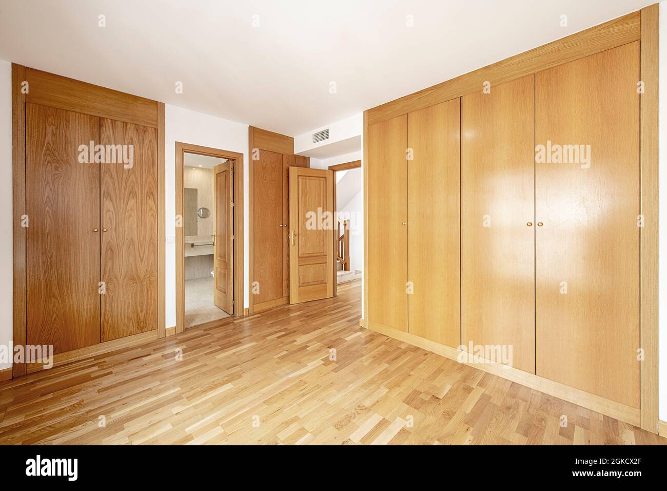Empty en-suite bedroom with oak cabinets, oak flooring, and oak doors and trim Stock Photo