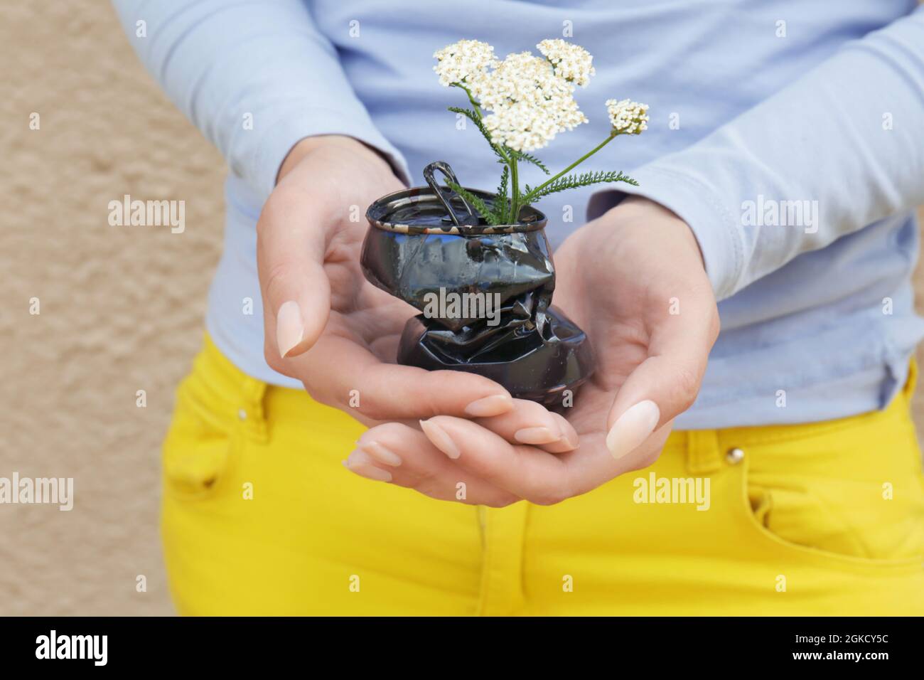 Woman holding crushed tin can with flower on color background. Recycling garbage concept Stock Photo
