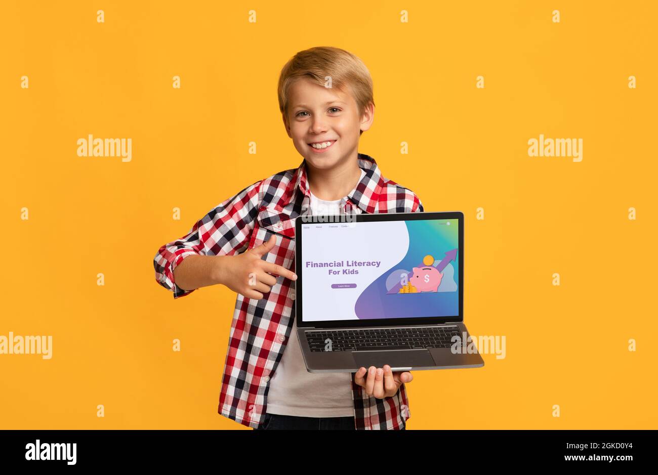 Smiling Caucasian boy pointing at laptop screen with Financial Literacy For Kids school website, orange background Stock Photo