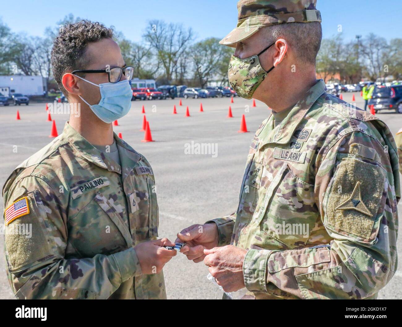 U.S. Army Pfc. Wascar Paulino, a combat medic with 1st Battalion, 7th Field Artillery Regiment, 2nd Armored Brigade Combat Team, 1st Infantry Division, receives a military coin from U.S. Army Lt. Gen. Robert “Pat” White, III Armored Corps and Fort Hood, Texas, commanding general, at the Fair Park Community Vaccination Center (CVC) in Dallas, March 17, 2021. White thanked Paulino for his work ethic and his role in assisting the Federal Emergency Management Agency (FEMA) in its national vaccination efforts. U.S. Northern Command, through U.S. Army North, remains committed to providing continued, Stock Photo